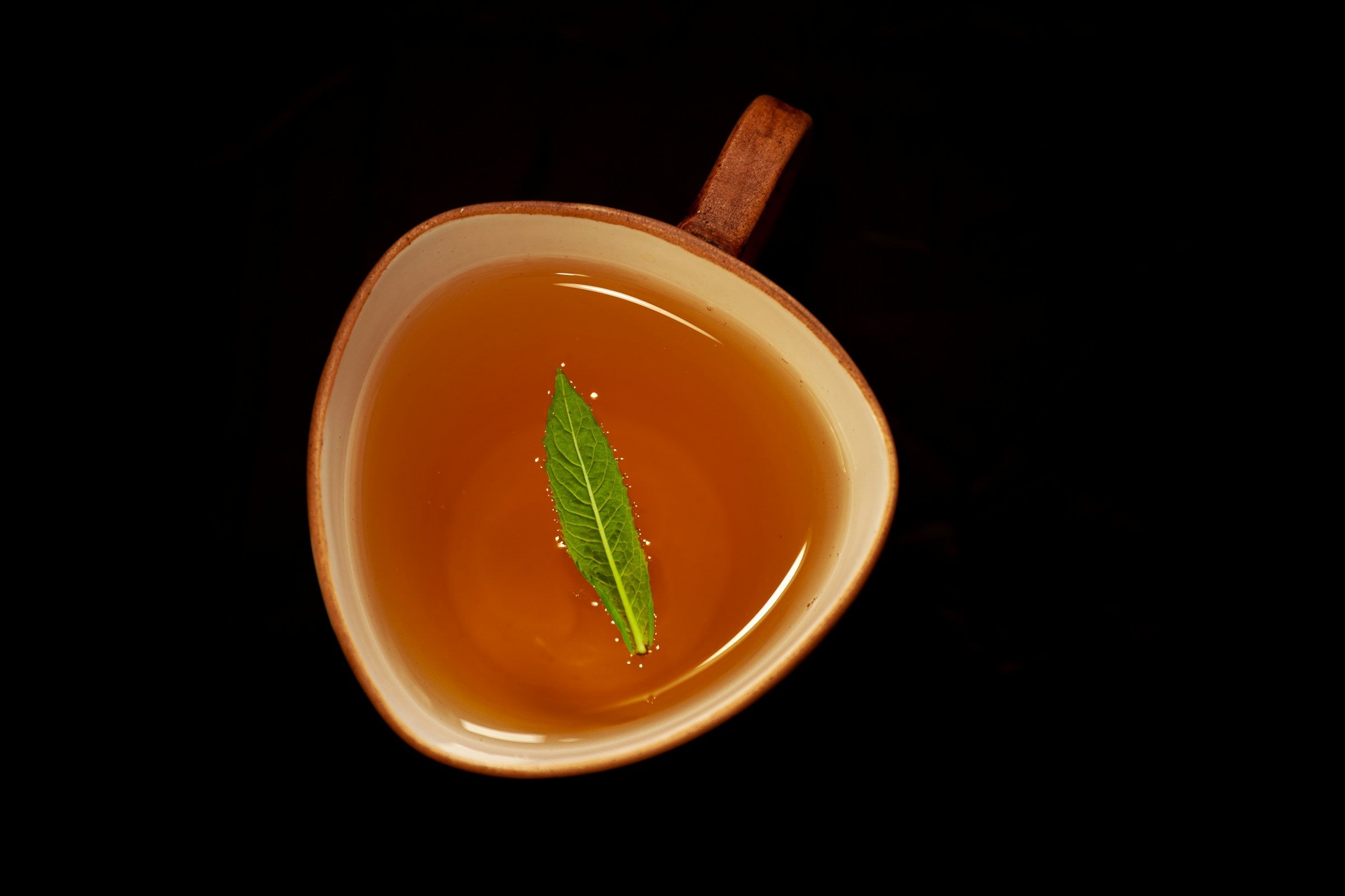 Mintora mint and herb aroma tea in a warm ceramic cup with a fresh mint leaf floating on top, set against a dark background